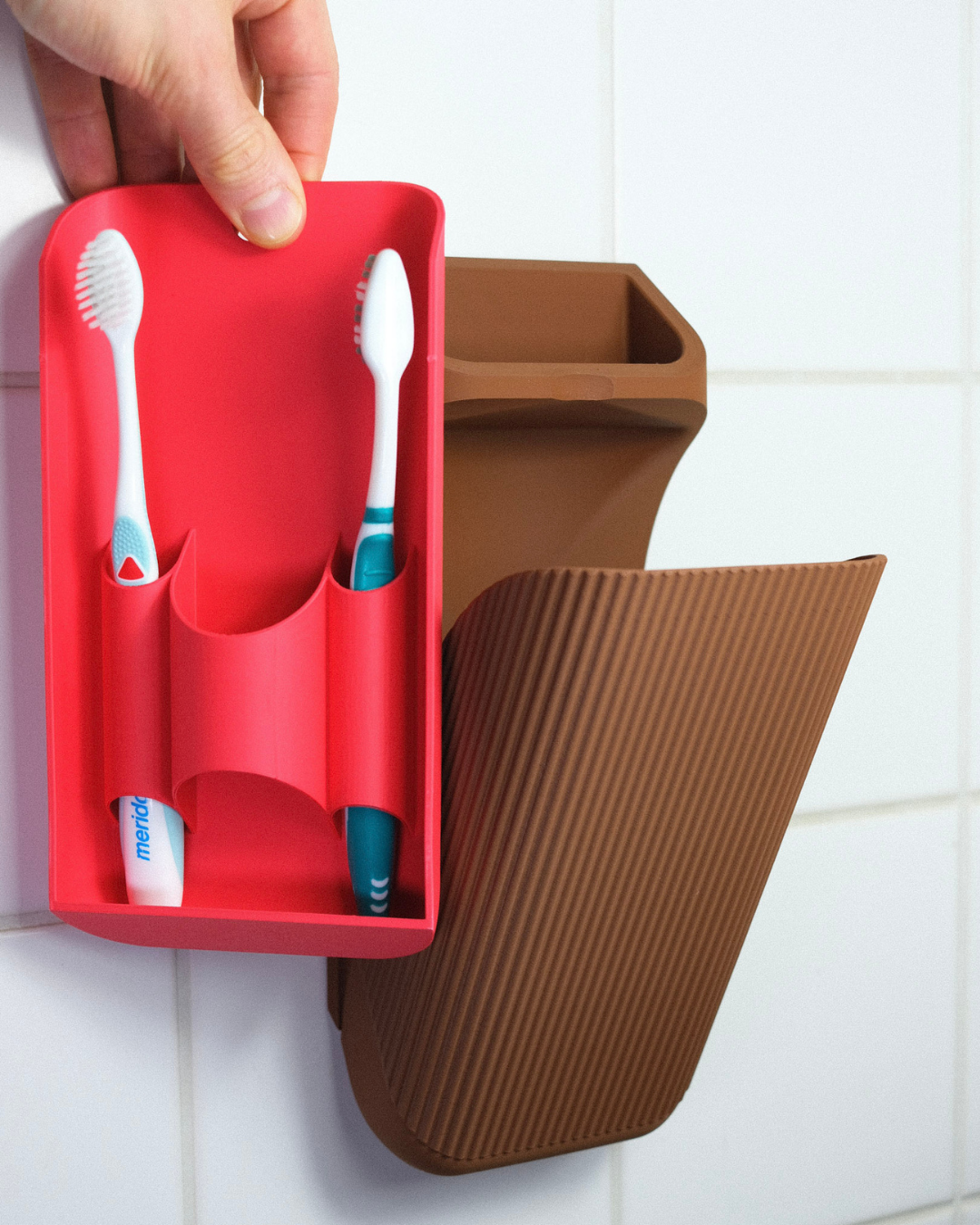 Red toothbrush holder with two toothbrushes on a tiled bathroom wall.